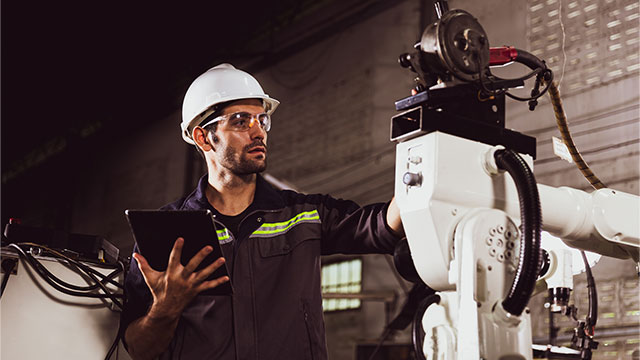 Engineer using tablet to control welding robotic automatic arm machine.