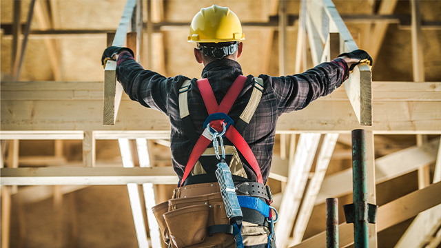 Carpentry worker wearing a harness and hard hat whilst on the top of framing