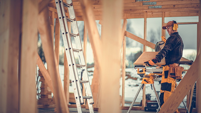 Carpentry male worker wearing protective equipment whilst working in house framing