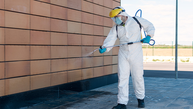 Cleaner wearing full suit high pressure cleaning outside of building