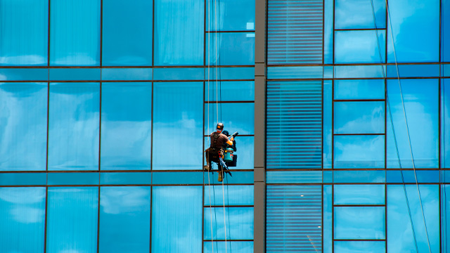 window cleaner on side of high rise building wearing a harness