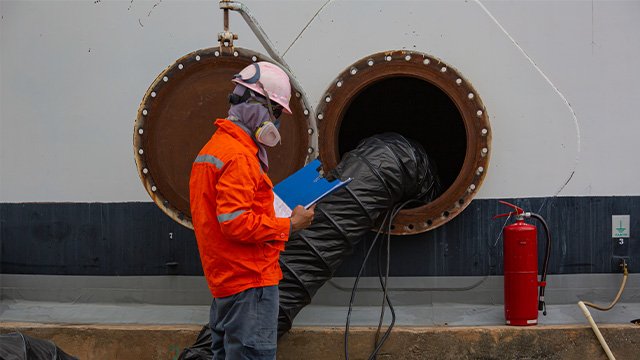 Worker wearing PPE whilst checking confined space documentation