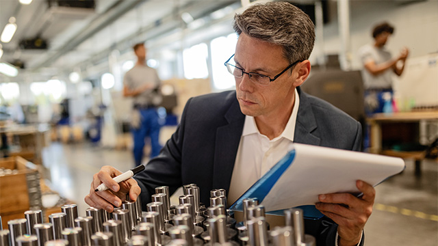 Manager checking quality of manufactured products with clipboard and pen in hand