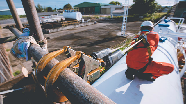 Lone gas engineer on the top of tank with two carabiner clips onto the top poles to ensure there are no falling injuries 