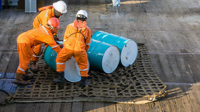 three chemical engineers working together to manual move three barrels