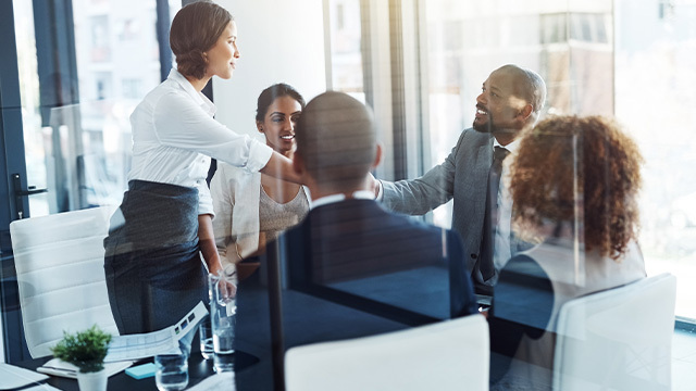 male and female coworkers sitting in the boardroom with two coworkers shaking hands